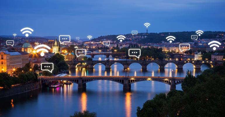 Lit buildings and bridges with connectivity icons in Prague, Czech Republic, at dusk.