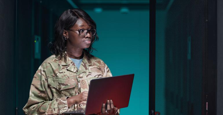 Waist up portrait of young African-American woman wearing military uniform using laptop while standing in server room.