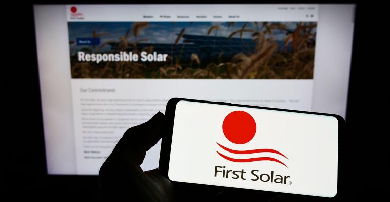 Person holding smartphone with logo of US renewable energy company First Solar Inc. on screen in front of website. Focus on phone display.