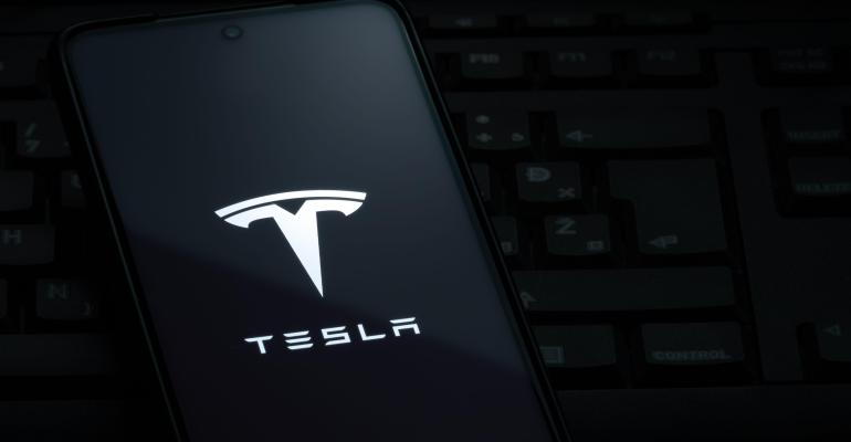 Tesla logo on smartphone screen laying on computer keyboard