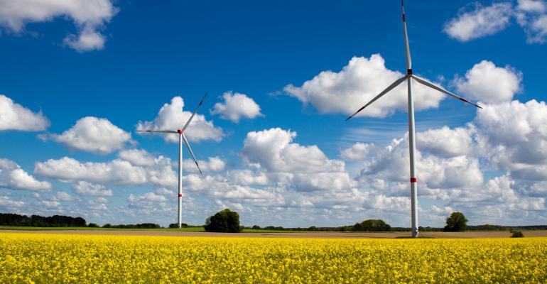 Two wind turbines with cloudy sky in the background and rapeseed field in the foreground