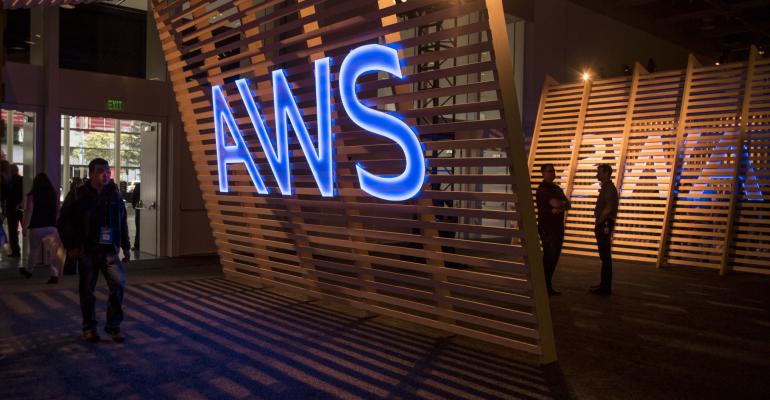 Image of AWS logo on wooden slat background as people walk by.