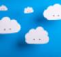 Cloud computing concept with white cardboard cutout cute clouds with eyes hanging in front of a sky blue background.