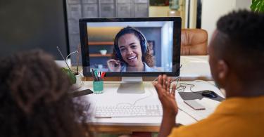 woman on a monitor on a conference call, with two in-office colleagues