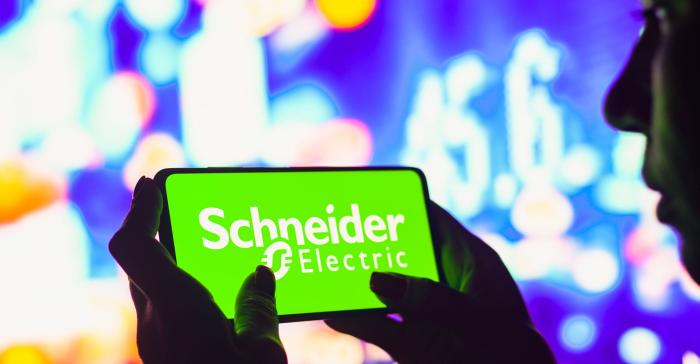 In this photo illustration, a silhouetted woman holds a smartphone with the Schneider Electric logo displayed on the screen. 
