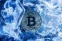 Photo of blue toned Bitcoin coin laying on cracked ice surface. 