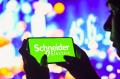 In this photo illustration, a silhouetted woman holds a smartphone with the Schneider Electric logo displayed on the screen. 