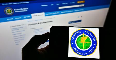 Person holding smartphone with seal of US agency Federal Aviation Administration (FAA) on screen in front of website.