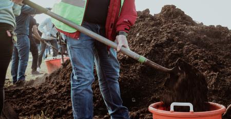 image of volunteer shoveling soil into a bucket in foreground with other volunteers shoveling in the background
