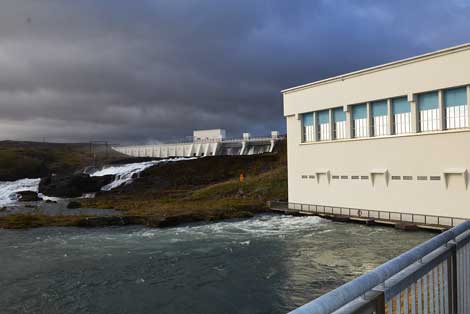 View of the Ljósafossstöð hydroelectric plant in Iceland. Water seen flowing over the dam, at left, while water used in the plant to spin turbines and create electricity is seen coming out from under building at right. The water is flowing from a spring-fed lake, Þingvallavatn, into rivers and streams.  (Photo by Colleen Miller)